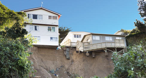 Two homes hanging over the edge of a slope after a landslide in Wellington.